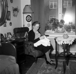 Vrouw zit met een handwerkje in een stoel voor het raam, Bestanddeelnr 252-9124