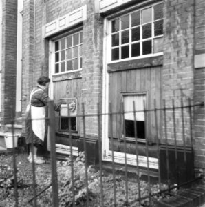 Vrouw wast ramen van een deels dichtgespijkerd kozijn, Bestanddeelnr 900-8486