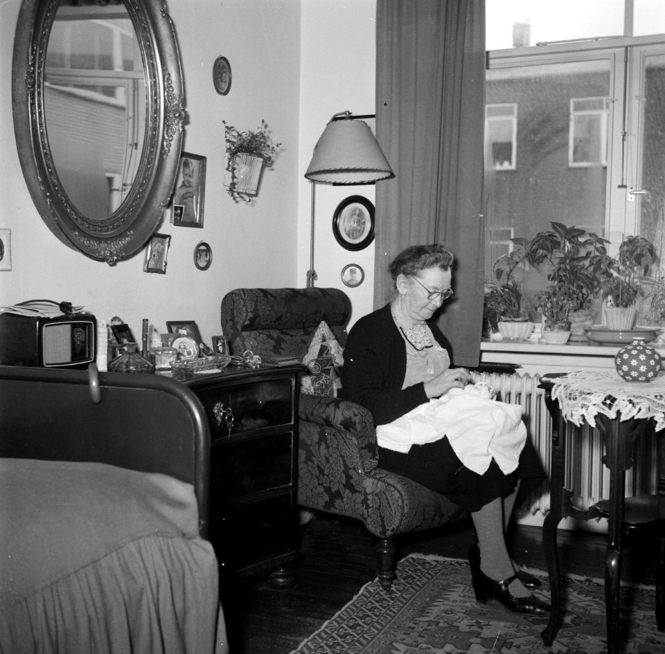 Vrouw zit met een handwerkje in een stoel voor het raam, Bestanddeelnr 252-9123