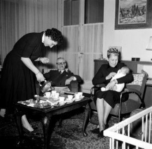 Vrouw bij het koffie inschenken voor de visite terwijl een dame de baby op schoo, Bestanddeelnr 252-9372