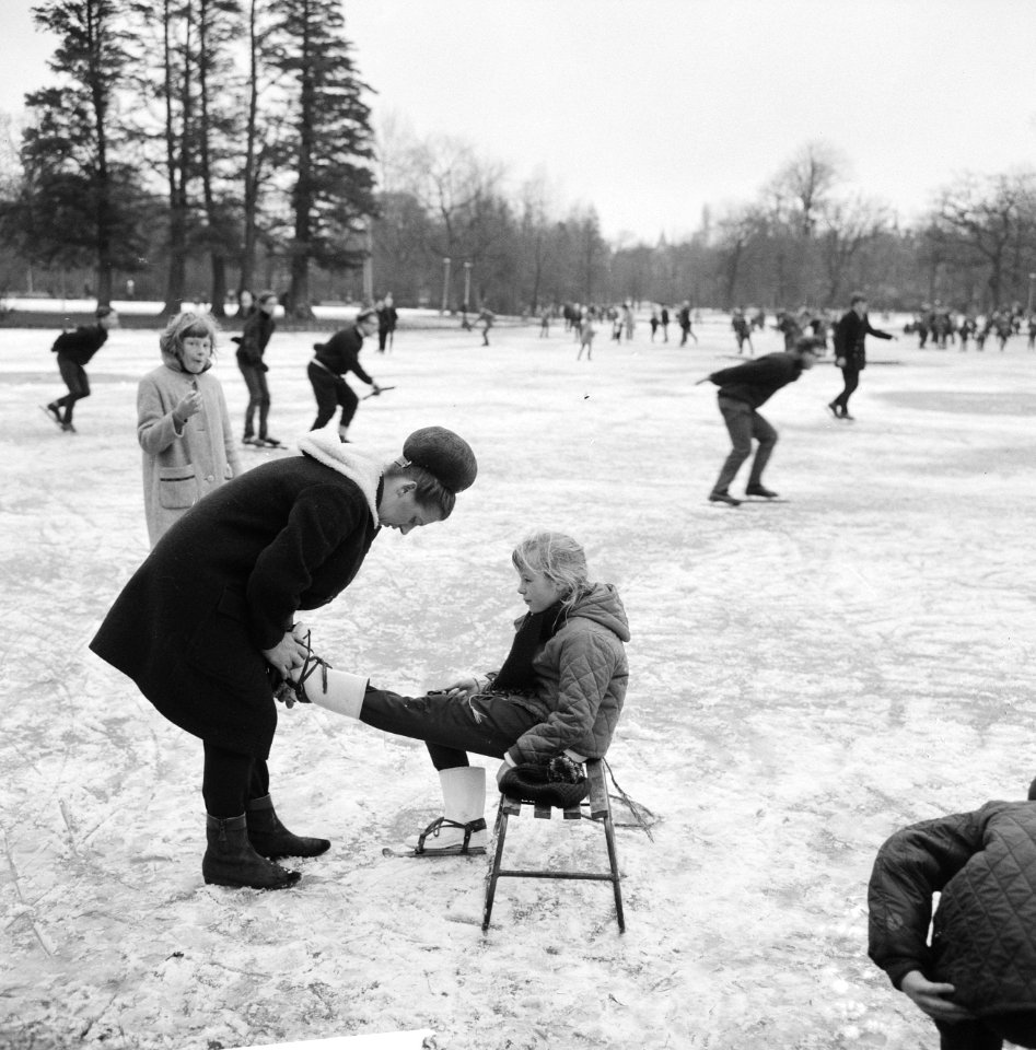 Vrouw terwijl zij schaatsen onderbindt bij een kind zittend op een sleetje, Bestanddeelnr 918-4692