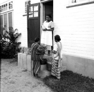 Vrouw met groentenverkoopsters aan de deur, waarschijnlijk in Paramaribo, Bestanddeelnr 252-2186