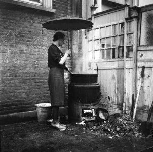 Vrouw met paraplu kookt wasgoed op een buitenfornuis Het gebouw rechts is een , Bestanddeelnr 900-6399