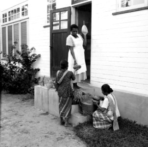 Vrouw met groentenverkoopsters aan de deur, waarschijnlijk in Paramaribo, Bestanddeelnr 252-2185