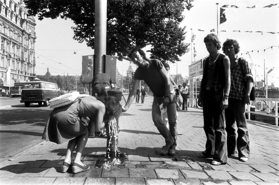 Voorbijgangers drinken water uit een pomp op het Damrak, Bestanddeelnr 928-0825