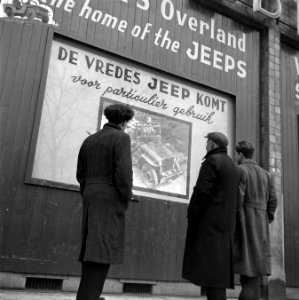 Voorbijgangers bekijken een poster met de tekst De Vredes Jeep Komt, Bestanddeelnr 901-2396