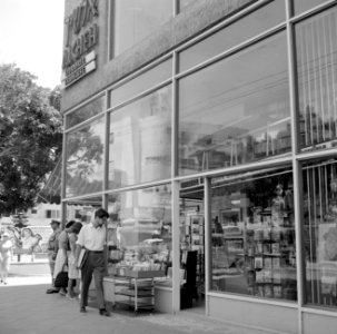 Voorbijgangers kijken geïnteresseerd in de etalage van een boekwinkel, Bestanddeelnr 255-1851