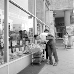 Voorbijgangers kijken geïnteresseerd in een kar met boeken voor de etalage van e, Bestanddeelnr 255-1856