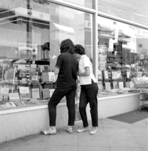 Voorbijgangers kijken geïnteresseerd in de etalage van een boekwinkel, Bestanddeelnr 255-1853