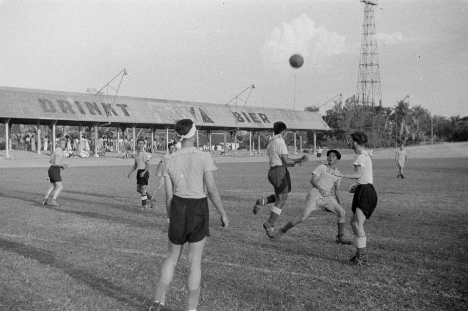 Voetbalwedstrijd. Het stadion heeft kunstlicht en een wielerbaan. Op het dak van, Bestanddeelnr 351-1-1