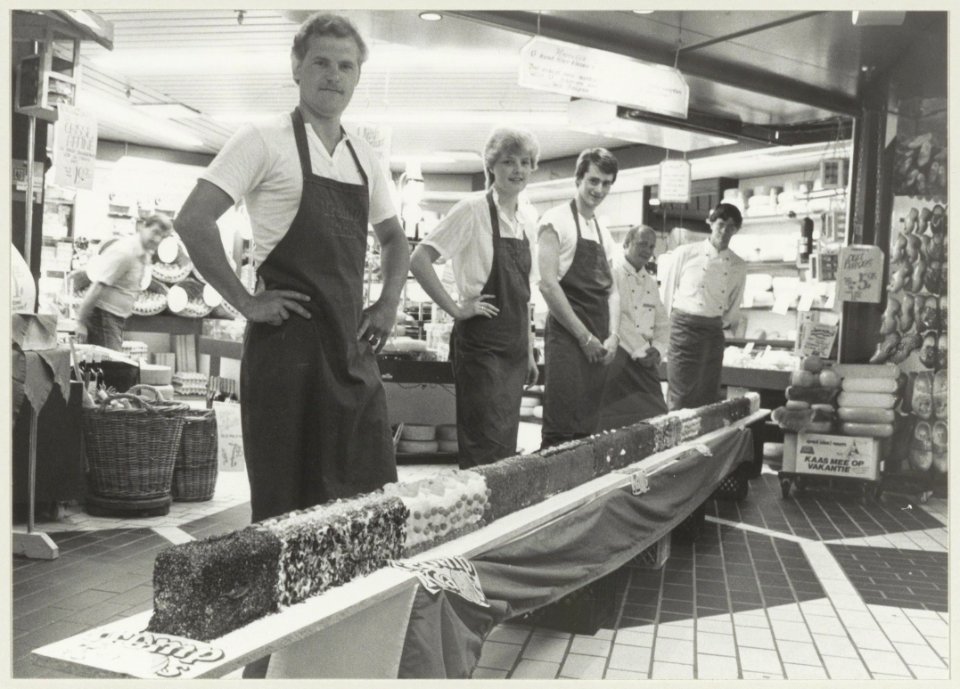 Werknemers van de kaashandel R. Tromp, met een zelfgemaakte kaas van 7 meter lengte. NL-HlmNHA 54013929