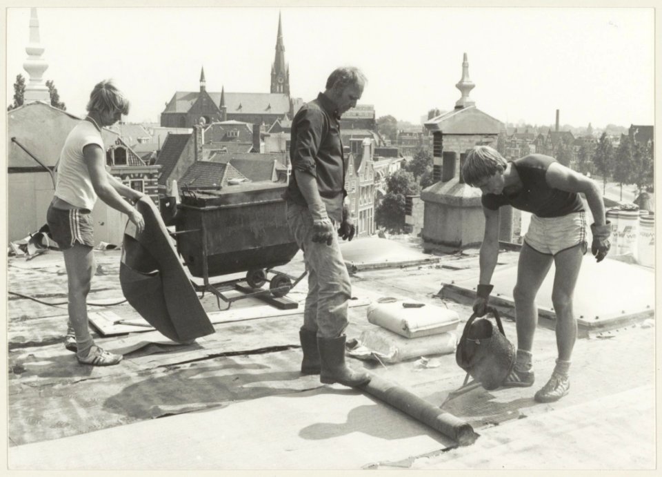 Werknemers van het dakdekkersbedrijf Nouris aan het werk op daken van huizen aan het Spaarne. NL-HlmNHA 54013230