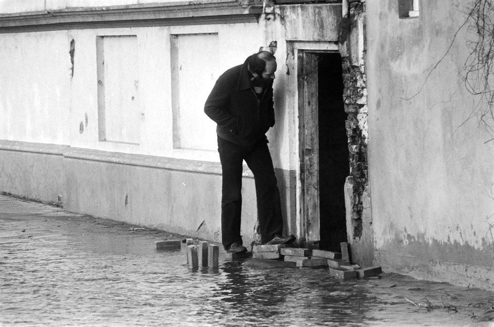 Wateroverlast door smelt- en regenwater. Man bij huis in ondergelopen straat, Bestanddeelnr 931-8990