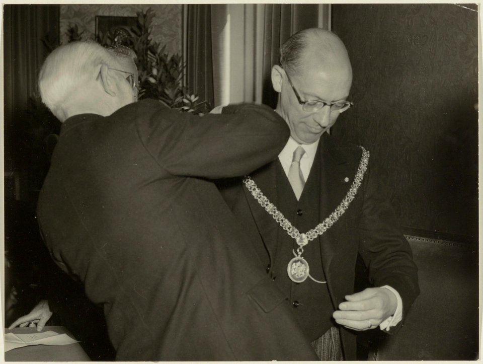 Wethouder Van Geluk hangt de nieuwe burgemeester van Bloemendaal, D.H.Peereboom Voller, de ambtsketting om. NL-HlmNHA 54004561