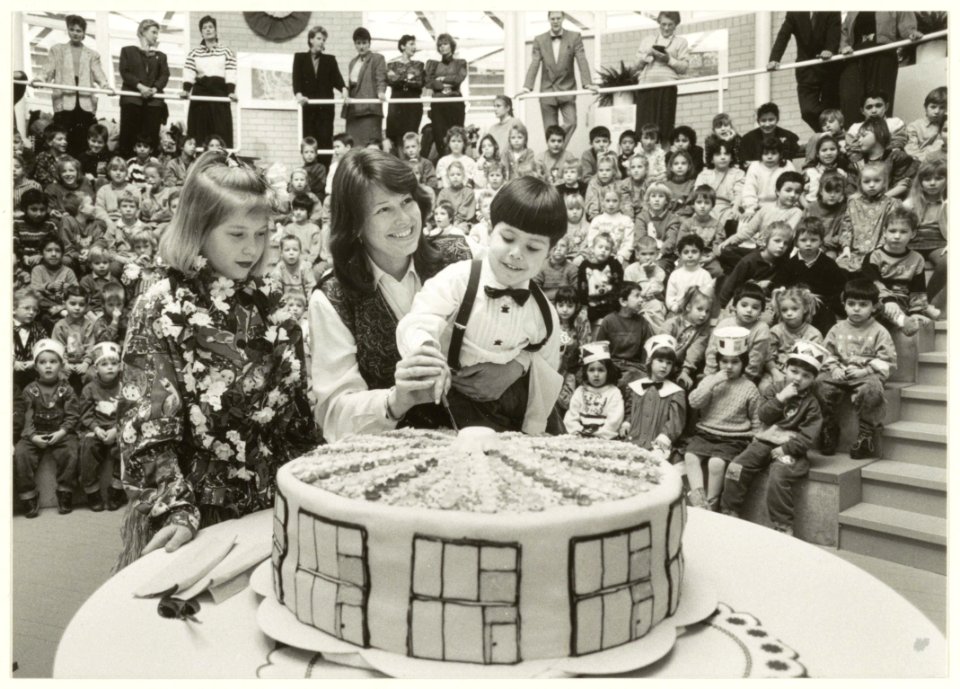 Wethouder Loeki van Balen, samen met leerlingen, bij de opening van de nieuwe Zuiderpolderschool aan de Vrijheidsweg. De taart heeft dezelfde vorm als de school. NL-HlmNHA 54031427