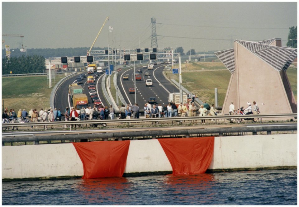 Zicht vanaf het tunneldak van de Wijkertunnel, waaraan een enorme oranje strik is bevestigd die door een helicopter zal worden weggetrokken, bij de feestelijke opening voor het eerste verkee, NL-HlmNHA 54036347
