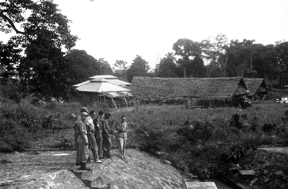 Zes militairen staan op een gemetselde waterkering. In de achterrond loodsen, Bestanddeelnr 6696
