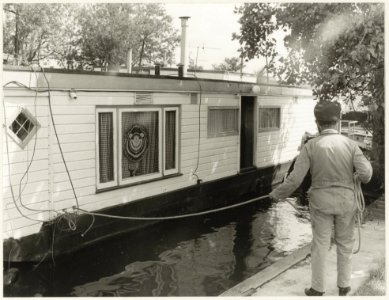 Woonboot wordt versleept met hulp van iemand van de Havendienst. NL-HlmNHA 54003425