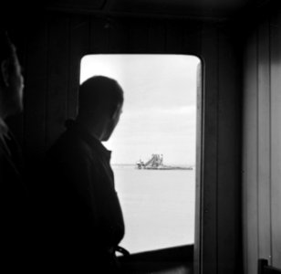 Bemanningslid van een schip kijkt uit de kajuit naar een baggermolen in de haven, Bestanddeelnr91-0913