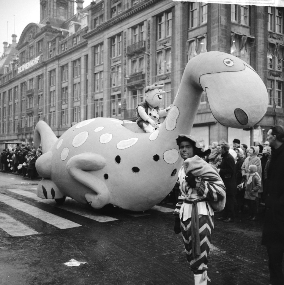 Zwarte Piet poserend voor een rijdende Dino met op zijn rug Barney Rubble ui, Bestanddeelnr 918-4674