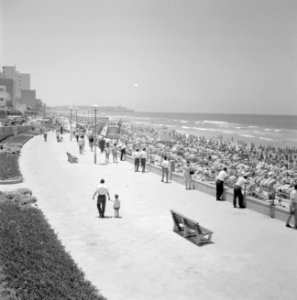Zomers geklede mensen lopen over de boulevard langs het drukbezochte strand, Bestanddeelnr 255-1946