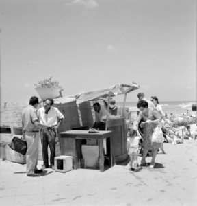 Zomers geklede mensen eten meloen aan de rand van het strand bij een eenvoudig k, Bestanddeelnr 255-1940