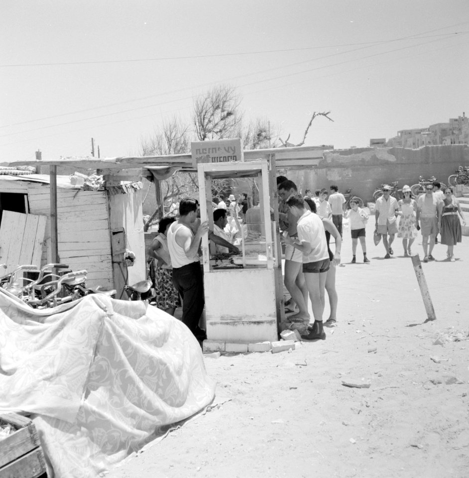 Zomers geklede mensen kopen eten aan de rand van het strand bij een kraampje dat, Bestanddeelnr 255-1941