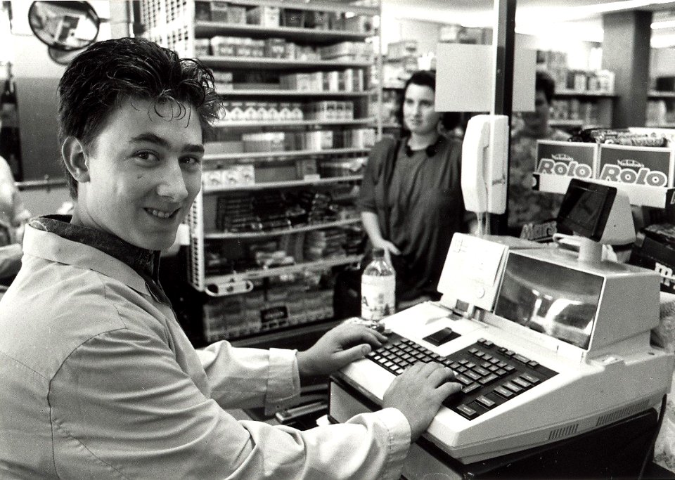 Albert Heijn vacantiewerker 16-jarige Barry van der Schuit achter de kassa. Aangekocht van United Photos de Boer bv. - Negatiefnummer 34691 k 2. - Gepubliceerd in het Haarlems Dagblad van 11.07.1991