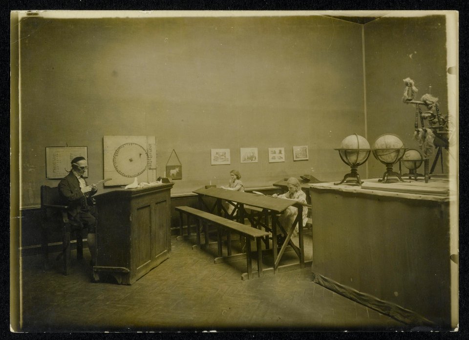 Interieur van een school met onderwijzer en twee meisjes leerlingen in een muse, Bestanddeelnr 158-0657