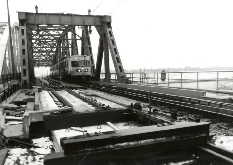 HUA-170384-Gezicht op de spoorbrug over de IJssel te Zutphen, met een passerend diesel-electrisch treinstel DE 2 ("Blauwe Engel") van de N.S., tijdens de werkzaamheden voor het leggen van het tweede spoor over d