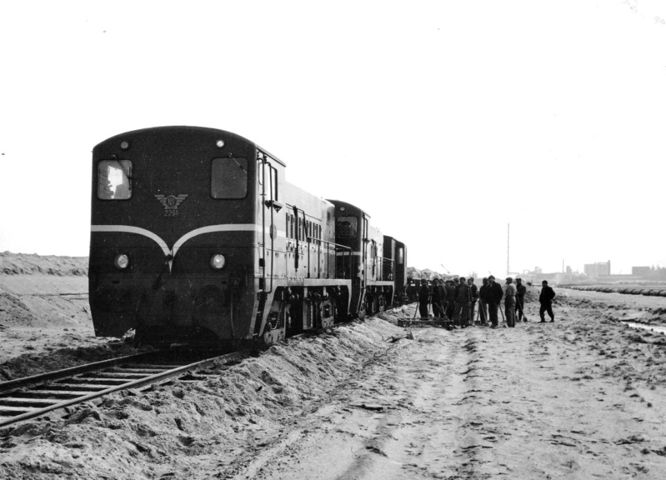 HUA-171034-Afbeelding van een goederentrein met stenen, getrokken door twee diesel-electrische locomotieven uit de serie 2200-2300 (voorop de 2261) van de N.S. ten behoeve van de aanleg van de Europoorthaven bij