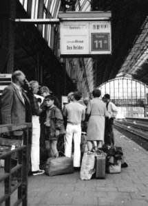 HUA-171283-Afbeelding van wachtende treinreizigers op het perron langs spoor 11 van het N.S.-station Amsterdam C.S. te Amsterdam, met een centrale treinaanwijzer (CTA)