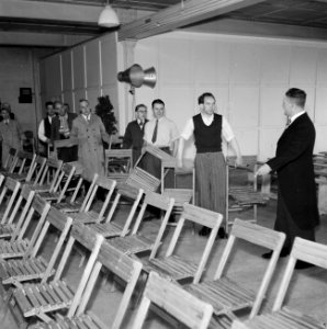 Man in jacquet geeft aanwijzingen aan mannen die stoelen klaar zetten, Bestanddeelnr 255-8543