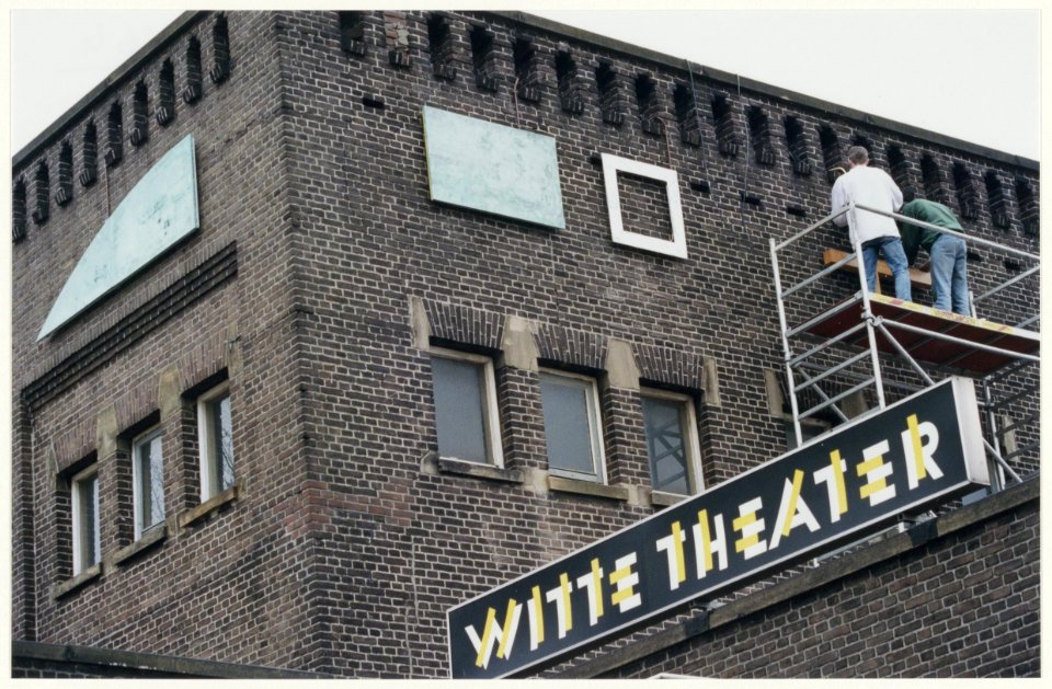 Kunstenaar Pieter Kooistra bevestigd een ornament van zijn kunstwerk aan de gevel van het Witte Theater in IJmuiden. NL-HlmNHA 54050081