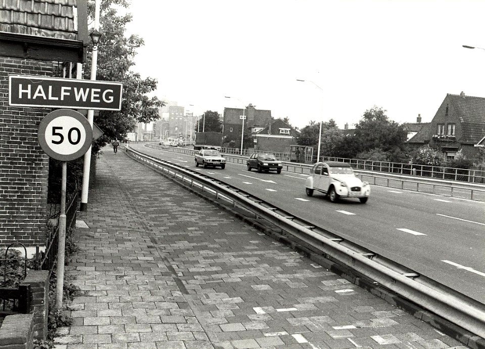 Dr. Baumannplein Amsterdamsestraatweg. De snelweg Amsterdam-Haarlem, dwars door Halfweg, ziende naar het westen. Aangekocht in 1985 van fotograaf C. de Boer. - Negatiefnummer 24282 k 5 A. - Gepublicee