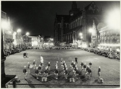Een drumband die deelneemt aan een marswedstrijd op de Grote Markt bij avondlicht, NL-HlmNHA 54011837
