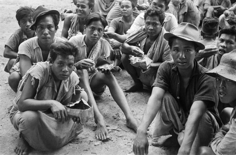 Een groep boeren of landarbeiders zit langs een weg. Zij eten van bananenbladere, Bestanddeelnr 470-5-3