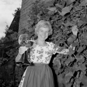 Erika Klein poseert met glas moezelwijn voor een muur begroeid met druiven, Bestanddeelnr 254-4641