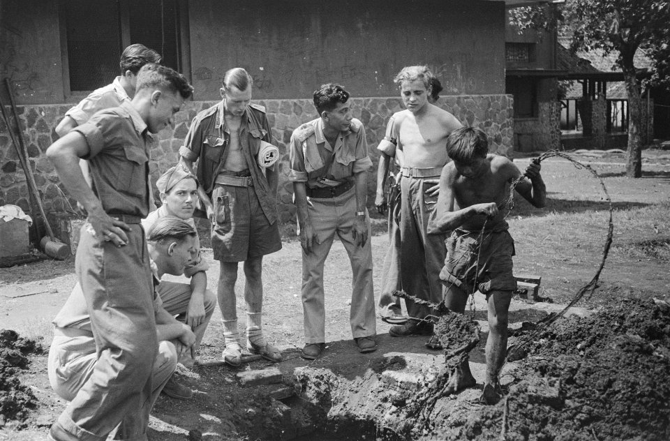 Een man haalt een kabel uit een gegraven gat terwijl Nederlandse militairen om, Bestanddeelnr 32-3-3