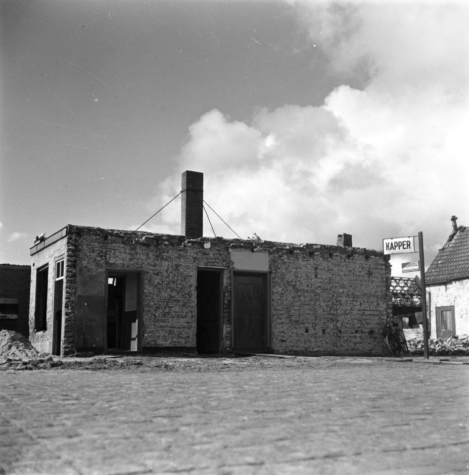 Een zwaar beschadigd gebouw met een uithangbord 'kapper, Bestanddeelnr 901-4648