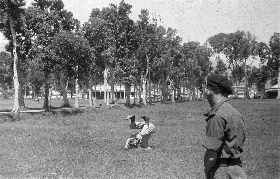 Militair maakt koprol op grasveld. Achter hem een pad omzoomd met bomen. Op de v, Bestanddeelnr 334-1-3