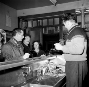 Mensen tijdens het drinken van een glaasje aan de bar terwijl de barkeeper insch, Bestanddeelnr 252-9494