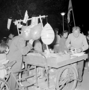 Verkoper en klanten bij feestelijk versierde fietskar met hapjes, Bestanddeelnr 255-1928