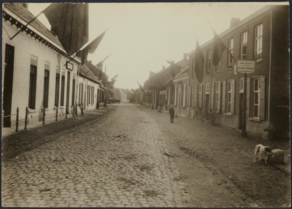 Straat in Belgische stad met vlaggen aan de huizen en een bord met opschrift R, Bestanddeelnr 158-1748