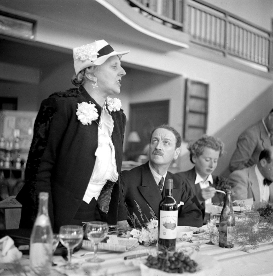 Vrouw met witte hoed en een corsage houdt een toespraak tijdens een diner, Bestanddeelnr 254-5394