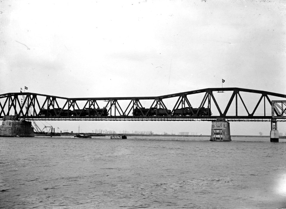HUA-166381-Gezicht op de van oorlogsschade herstelde spoorbrug over de Maas bij Hedel, met enkele Duitse stoomlocomotieven tijdens een belastingproef