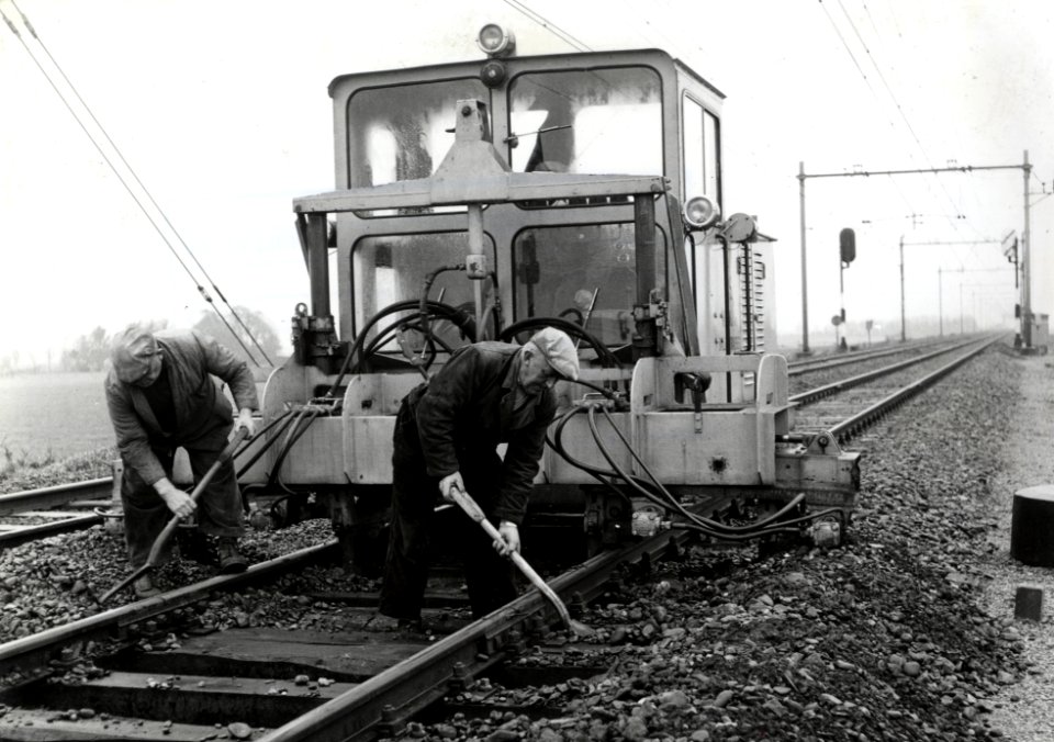HUA-169663-Afbeelding van de hormachine van de NS tijdens onderhoudswerkzaamheden aan de spoorlijn te Heerhugowaard met op de voorgrond twee wegwerkers