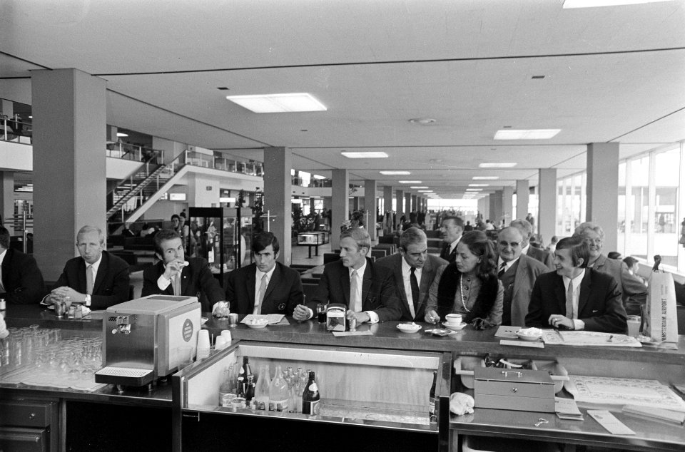Enkele spelers staan aan een bar tijdens het wachten op Schiphol, Bestanddeelnr 921-6830
