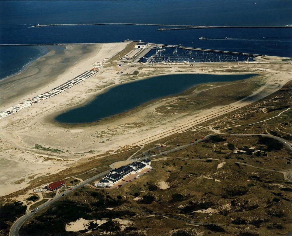 Enkele jaren geleden was dit één grote zandvlakte. Nu ligt er een nieuwe duinenrij aan zeezijde, een jachthaven met boulevard- en een binnenmeer. op de voorgrond een appartementencomplex en restaurant