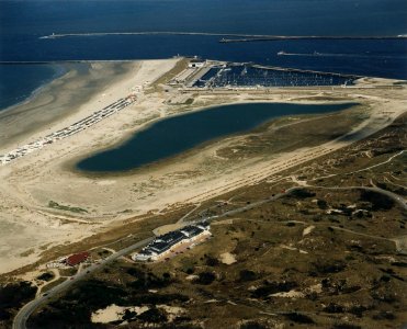 Enkele jaren geleden was dit één grote zandvlakte. Nu ligt er een nieuwe duinenrij aan zeezijde, een jachthaven met boulevard- en een binnenmeer. op de voorgrond een appartementencomplex en restaurant